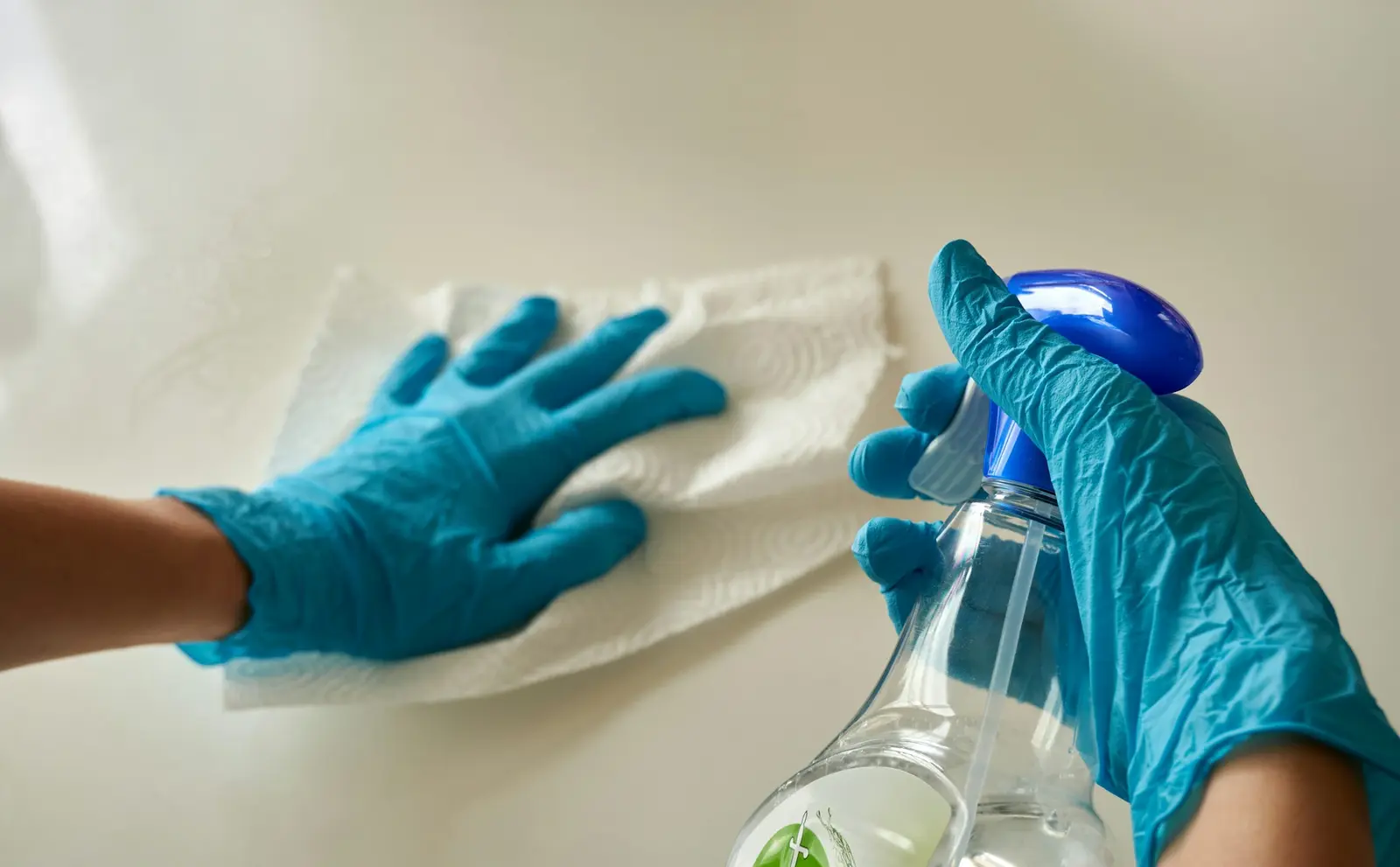 Gloved hand wiping a surface with disinfectant spray